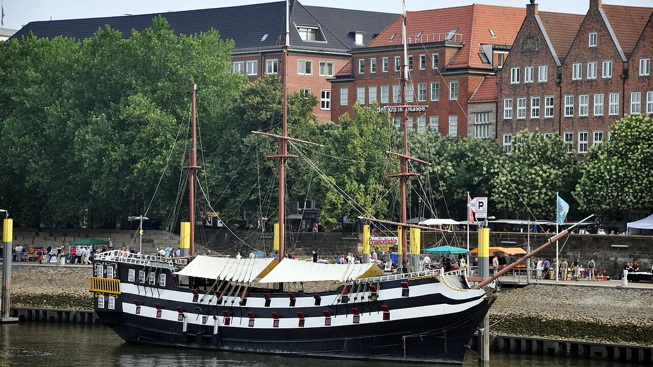 Nachbau eines Segelschiffs an der Schlachte in Bremen, dahinter Uferpromenade, Bäume und Backsteinhäuser
