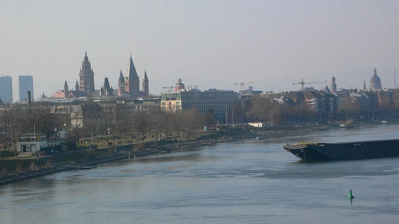 Blick über den Rhein auf die Mainzer Altstadt mit den roten Türmen des Doms, im Vordergrund ein Lastkahn